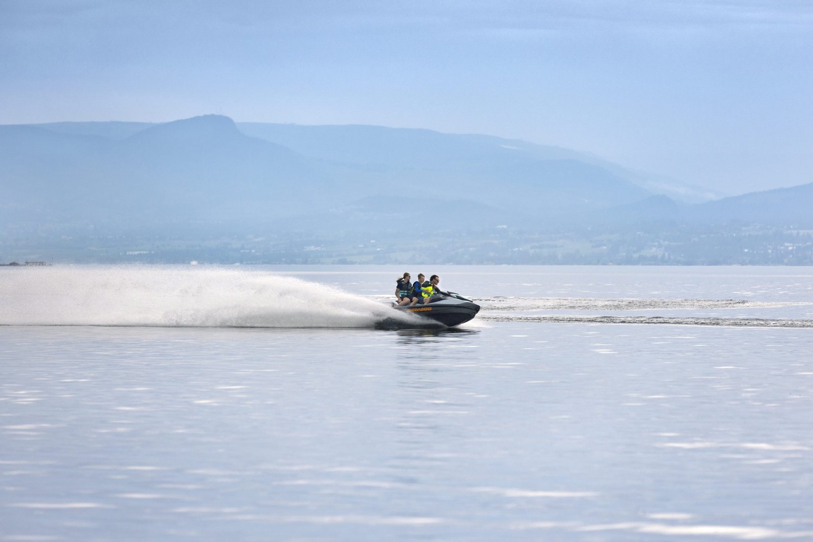 Motorbåt med tre personer som kjører på sjøen med fjell i bakgrunnen.
