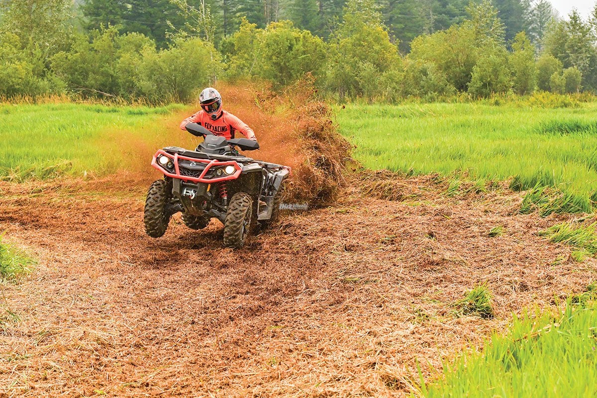 Kjøring på ATV i ujevnt terreng med natur- og fritidsaktiviteter, med grønt område og skog i bakgrunnen.
